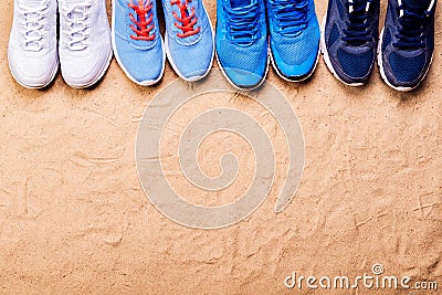 Various sports shoes in a row against sand, studio shot Stock Photo