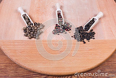 Various whole peppercorns in different wooden spice spoons and beside Stock Photo