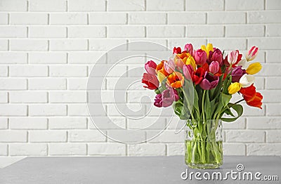 Vase with beautiful spring tulip flowers on table near brick wall. Stock Photo