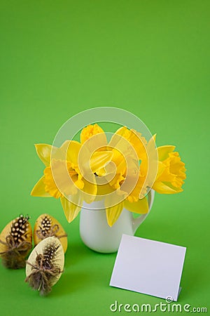 Vase with yellow daffodils next to decorated Easter eggs on a green background with post card Stock Photo