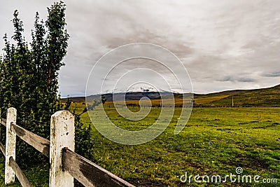 Vast green valley with a wooden fence mountains and a cloudy sky Stock Photo