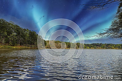 A vast rippling lake surrounded by lush green trees with a blue aurora lights in the sky at Murphey Candler Park Stock Photo