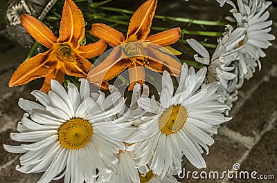 Orange lilies with decorative large daisies in a crystal vase on a brick wall Stock Photo