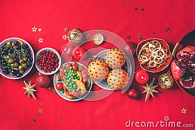 Vegan Christmas appetizers, olive, orange, fruits, vegetable salads, candles, tangerine, pomegranate, star glitter sparkles on red Stock Photo