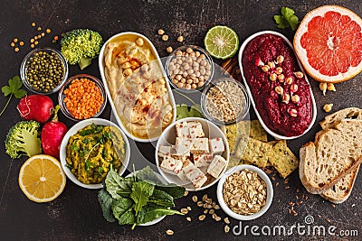 Vegan food background. Vegetarian snacks: hummus, beetroot hummus, green peas dip, vegetables, cereals, tofu. Top view, dark back Stock Photo