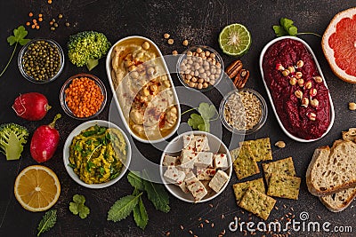 Vegan food background. Vegetarian snacks: hummus, beetroot hummus, green peas dip, vegetables, cereals, tofu. Top view, dark back Stock Photo