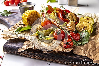 Vegan Grill menu, Grilled vegetables - zucchini, paprika, cherry tomatoes, corn, carrots and champignons served on wooden board at Stock Photo