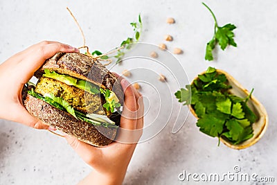 Vegan sandwich with chickpea patty, avocado, cucumber and greens in rye bread in children`s hands Stock Photo