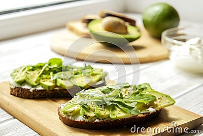 Vegan sandwich, rye bread toast, avocado slices, vegenaise sauce & raw arugula. Toasted sourdough, eggless mayonnaise, wooden tabl Stock Photo