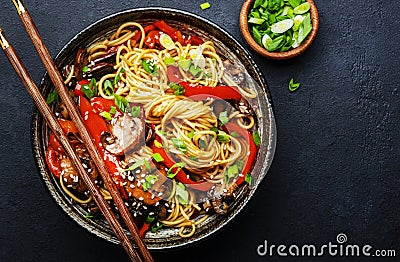 Vegan stir fry egg noodles with vegetables, paprika, mushrooms, chives and sesame seeds in bowl. Asian cuisine dish. Black table Stock Photo