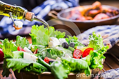 Vegetable lettuce salad. Olive oil pouring into bowl of salad. Italian Mediterranean or Greek cuisine. Vegetarian vegan food Stock Photo