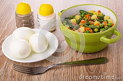 Vegetable mix from green bean, green peas, potato, onion, carrot in bowl, salt, pepper shaker, boiled eggs in saucer, fork on Stock Photo