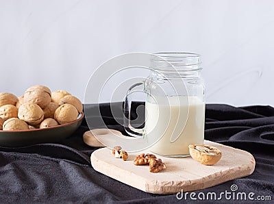 Vegetable walnut milk in a glass cup with a handle on a wooden cutting board. Walnuts in a plate in the background. Healthy drinks Stock Photo