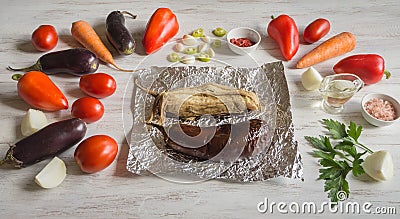 Eggplant baked on foil and vegetables are laid out on a wooden table. Vegetables on a light wooden background. Stock Photo