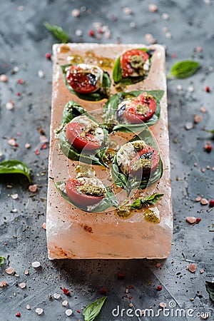 Vegetarian snack presented on pink salt block. Caprese salad with pesto sauce on basil leaves served on Himalayan salt block on Stock Photo