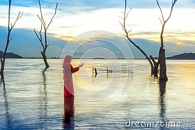 Veiled Islamic muslim woman wearing a burka standing and praying in the river Stock Photo