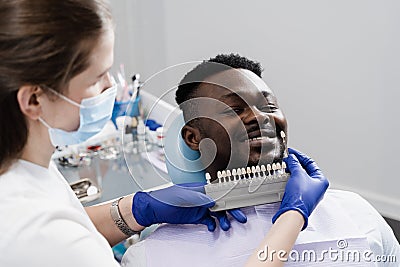 Veneers or implants teeth color matching samples for tooth whitening for african patient in dental clinic. Teeth color Stock Photo