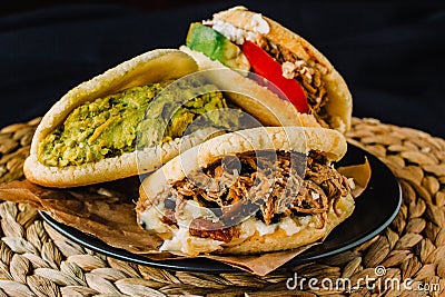 Venezuelan arepas on a black background, made with maize and filled with avocado, tomato, meat, cheese and black beans Stock Photo