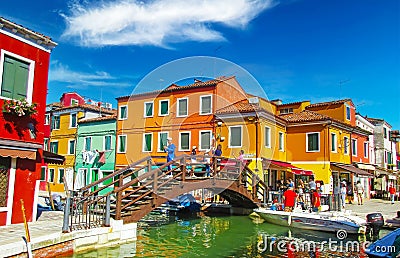 View on water canal with boats, wood bridge tre ponti, tourist crowd, gaudy brightly colored houses against blue sky, fluffy cloud Editorial Stock Photo