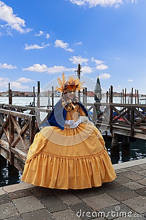 A participant in the Venice Carnival in an original yellow costume and mask poses on the embankment Editorial Stock Photo