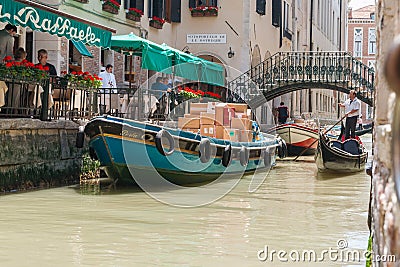 Goods and materials transported and delivered by boat in narrow canals with gondola and tourists Editorial Stock Photo