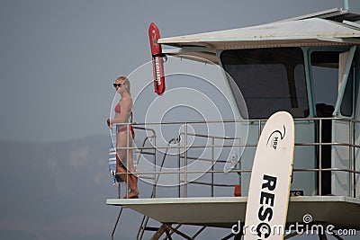 A female lifeguard at Ventura Harbor stands watch from a lifeguard tower at a breakwater Editorial Stock Photo