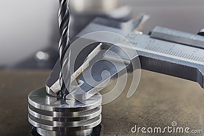 Vernier caliper measures metal drill bit, make holes in steel billet on industrial drilling machine. Metal work industry Stock Photo