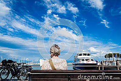 Verona, italy - september 21, 2021: A retired woman relaxes by reading a book sitting on a bench next to the promenade on a sunny Editorial Stock Photo