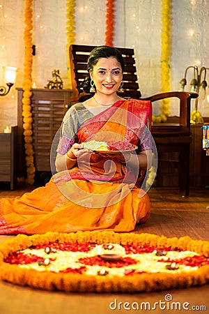 Vertcial shot of happy indian girl holding flower plate for diwali celebration by looking at camera at home - concept of Stock Photo