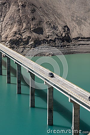 Vertical aerial drone shot of a bridge on the teal water at feet of hills with cars driving across Editorial Stock Photo