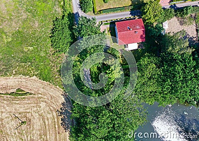 Vertical aerial view of a small hut with a red saddle roof on a country road with bushes and trees and a field and meadows in the Stock Photo