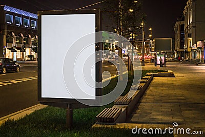 Vertical blank glowing billboard on night city street. In background buildings and road with cars. Mock up. Stock Photo