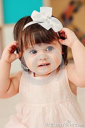 Vertical close up indoor portrait of cute happy baby girl playing with dressy white headband Stock Photo