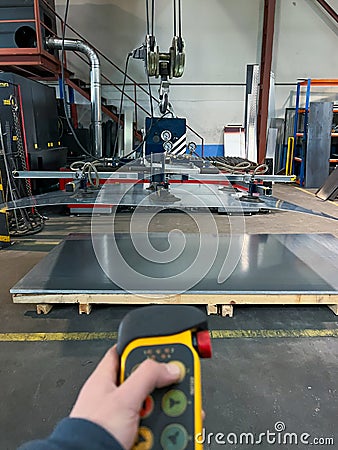 vertical close-up of an unrecognizable worker using a remote control to use the suction cup machine to transport large metal Stock Photo