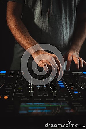 Vertical closeup of a DJ working under the lights against a dark background in a studio Stock Photo