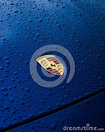 Vertical closeup of the Porsche 911 Carrera S front badge, blue car surface with water drops. Editorial Stock Photo