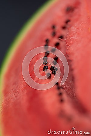 A vertical closeup portrait of the black seeds sitting in the pink red pulp of a cut slice of green watermelon. The piece of fruit Stock Photo