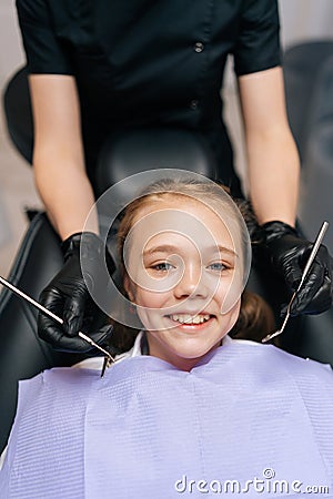 Vertical closeup portrait of happy cute little girl smiling looking at camera sitting in stomatology seat while dentist Stock Photo