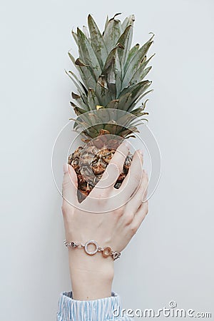 Vertical closeup shot of a female hand with a nice golden bracelet holding a whole pineapple Stock Photo