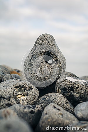 Vertical closeup shot of a pebble rock with a hole on a pile of rocks on a blurred background Stock Photo