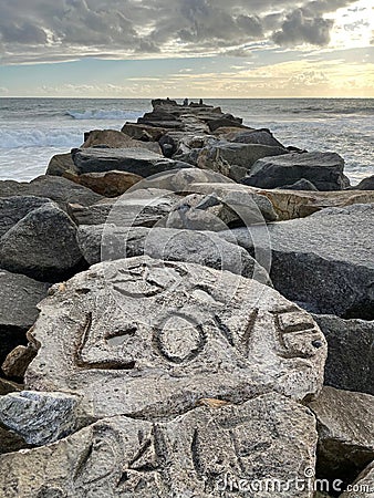 Vertical closeup of stone line carved the text "love", sea waves making foam, sunlit sky background Stock Photo