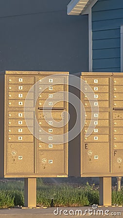 Vertical frame Row of mailboxes with numbers and compartments beside a road on a sunny day Stock Photo