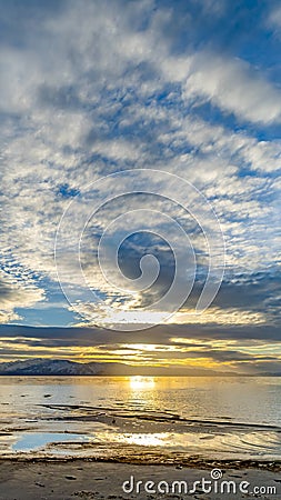 Vertical frame Striking cloudy sky over a calm lake that reflects the golden sun at sunset Stock Photo