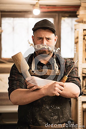 Vertical funny businessman, carpenter in cap, apron with shaving chip mustache under nose, holding chisel, mallet tools Stock Photo