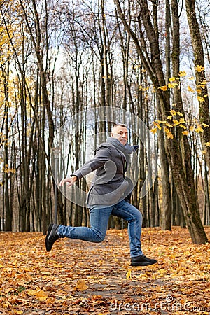 Vertical funny excited powerful mature grizzled businessman jump on one leg with raised leg and arms, levitating in park Stock Photo