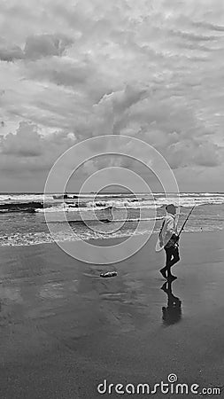 Vertical grayscale shot of a fisherman walking along a sandy shore Editorial Stock Photo