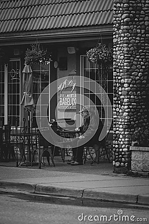 Vertical greyscale shot of an elderly male sitting in an outdoor bagel shop Editorial Stock Photo