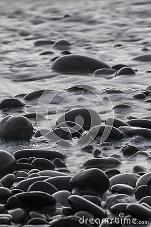 Vertical greyscale shot of pebbles in the water of the sea Stock Photo
