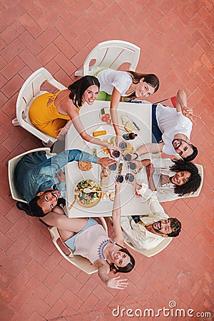 Vertical high angle top view of a group of best friends toasting wine glasses smiling and looking up to the camera Stock Photo