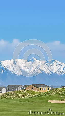 Vertical Homes and grassy field with snow covered mountain and blue sky background. Stock Photo